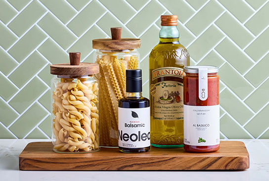 Gourmet olive oil, pastas & sauces arranged neatly on a cutting board in a kitchen.